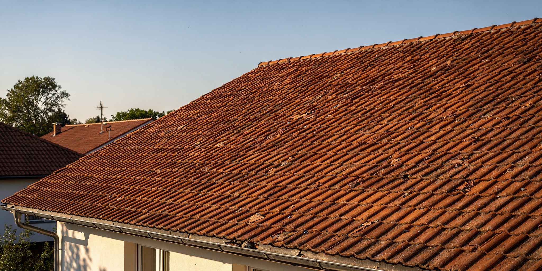 Katon korjaus variables[width=2048,height=1024,description=Photorealistic image from medium distance (showing some surroundings) of good condition clay tile roof OR metal sheet roof (choose one). Not too detailed. Natural daylight. No people, no text, no logos]