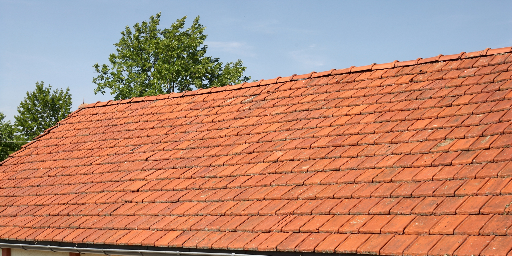 Katon korjaus variables[width=2048,height=1024,description=Photorealistic image from medium distance (showing some surroundings) of good condition tile roof OR metal sheet roof (choose one). Not too detailed. Natural daylight. No people, no text, no logos]